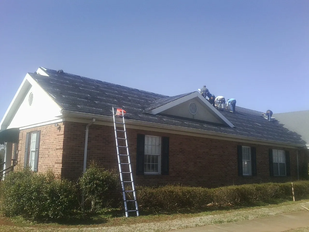 Crew tearing shingles off a brick ranch roof with a ladder set — Metal Roof Repair work by our crew in Sterling Forest
