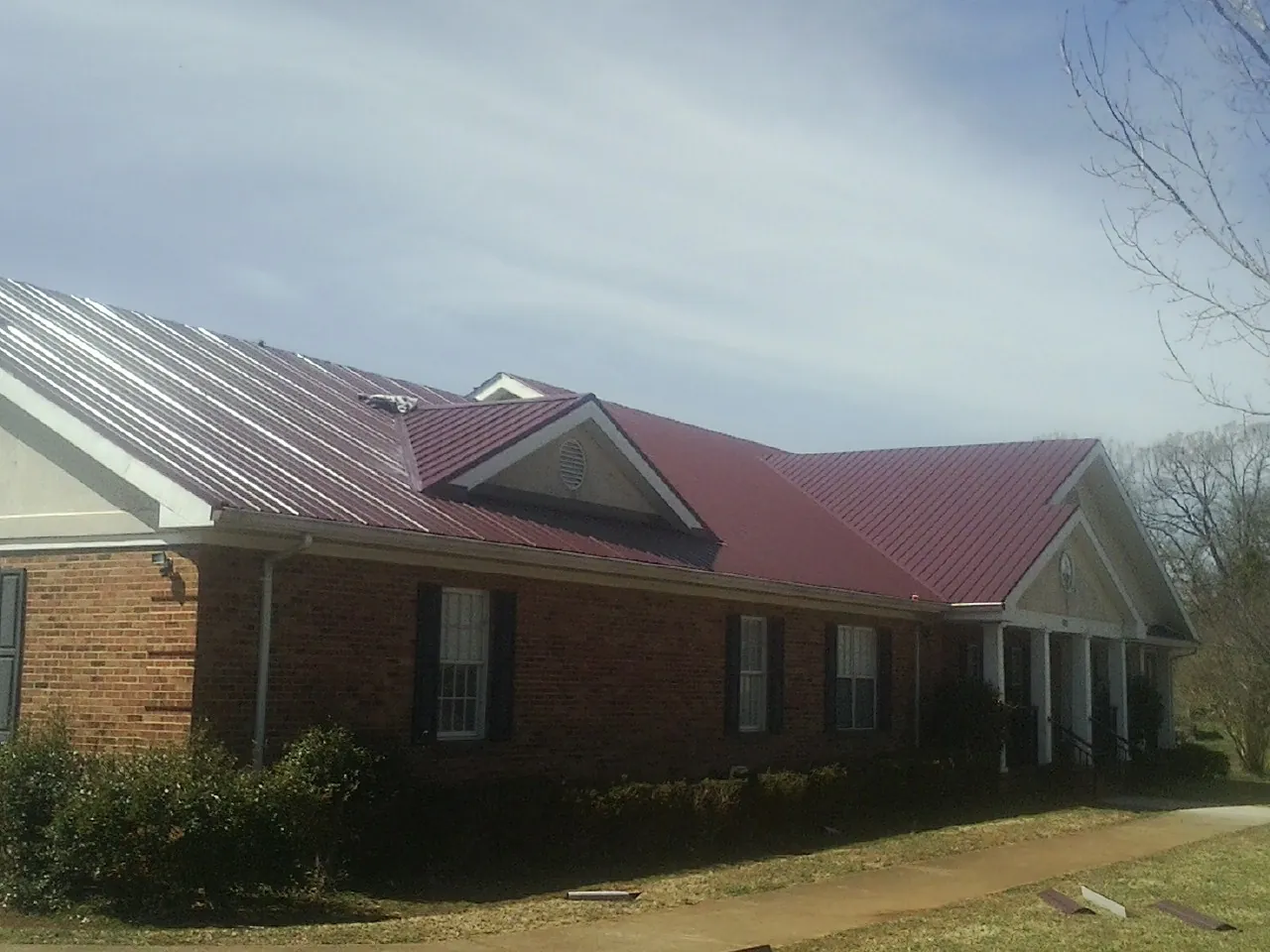 Red metal roof with gabled entries on a long brick building, from a Hail Damage Roof Repair job in Sterling Forest