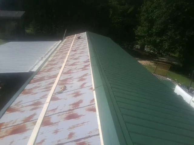 Old rusted panels beside newly installed green metal roofing — Wind Damage Roof Repair by Roofing Brothers in Sterling Forest