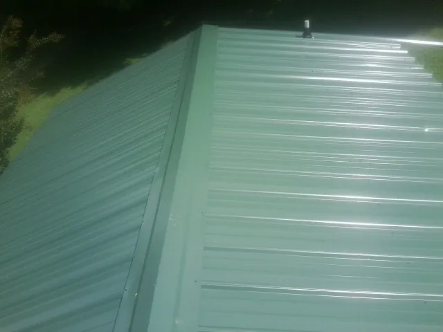 New green metal panels meeting at the ridge of a roof — Flat Roof Repair work by our crew in Sterling Forest