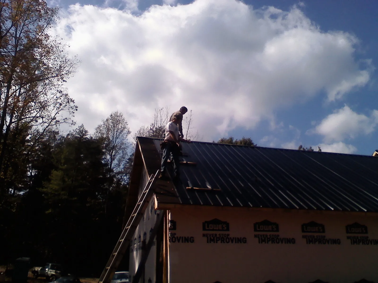 Roofer fastening dark metal panels high against a cloudy sky, from a Roof Inspection job in Sterling Forest