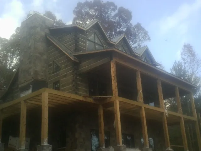 Stone chimney and dormers on a large log home with a timber porch in Sterling Forest