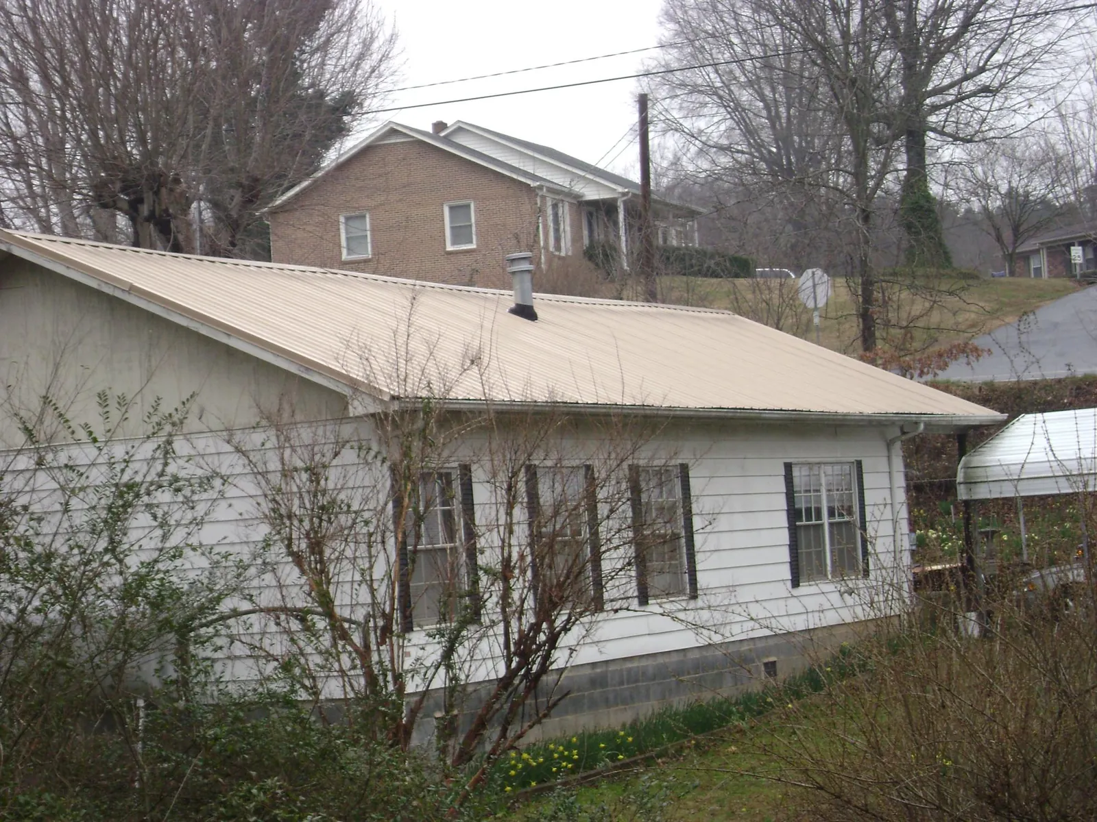 Tan metal roof on a white sided house set into a hillside — Commercial Roofing by Roofing Brothers in Sterling Forest