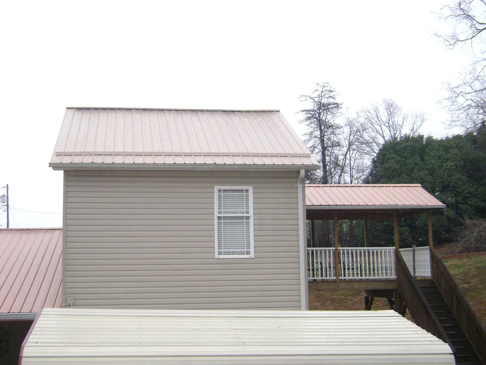 Tan metal roofs on a two story addition and attached porch, from a Roof Replacement job in Sterling Forest